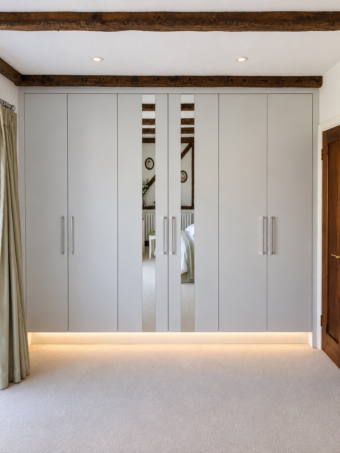 Matt white fitted wardrobes in Basildon showing symmetrical doors, vertical mirror strips and hidden plinth lighting