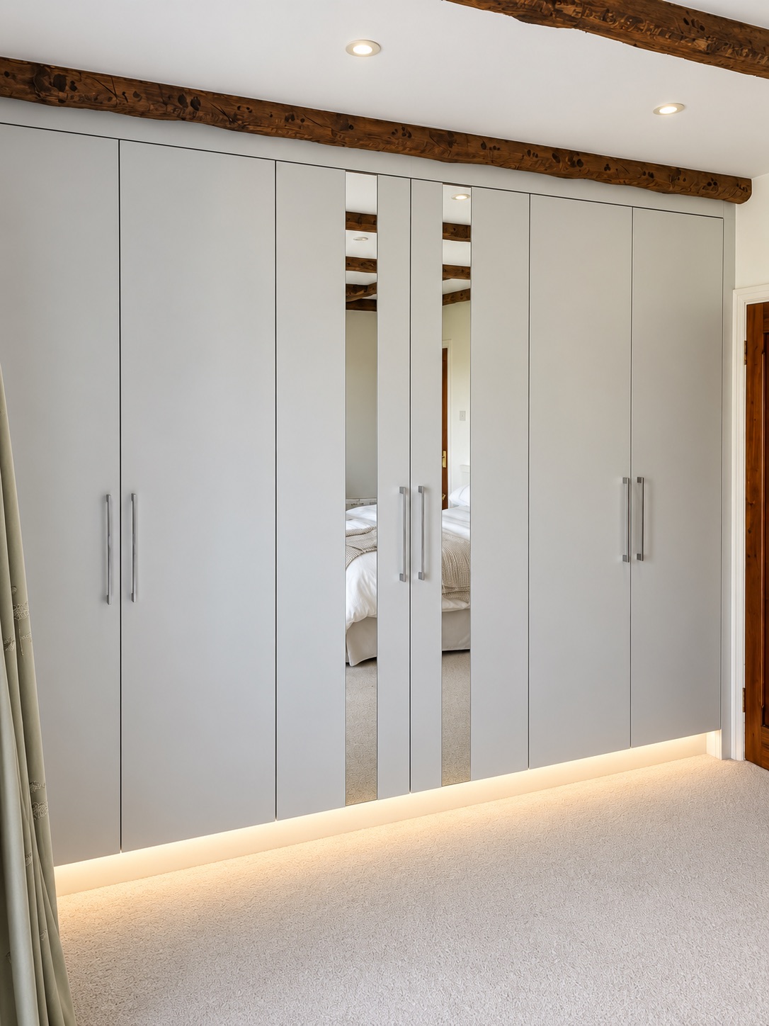 Matt white bespoke fitted wardrobes in Basildon with narrow vertical mirrored door panels and warm white plinth lighting