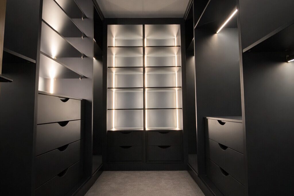 Black fitted wardrobe interior with LED lighting, drawers and display shelving for bags and shoes