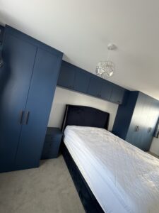 Modern fitted wardrobes around a bed with Tyrolean Blue doors, overbed storage and bedside unit
