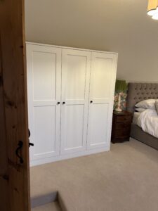 Custom corner wardrobe finished in Farrow and Ball All White with textured oak interiors, maximising bedroom storage.