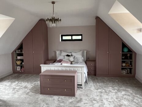 Rose pink built-in wardrobes with open display shelving in eaves space, designed for a cozy bedroom.