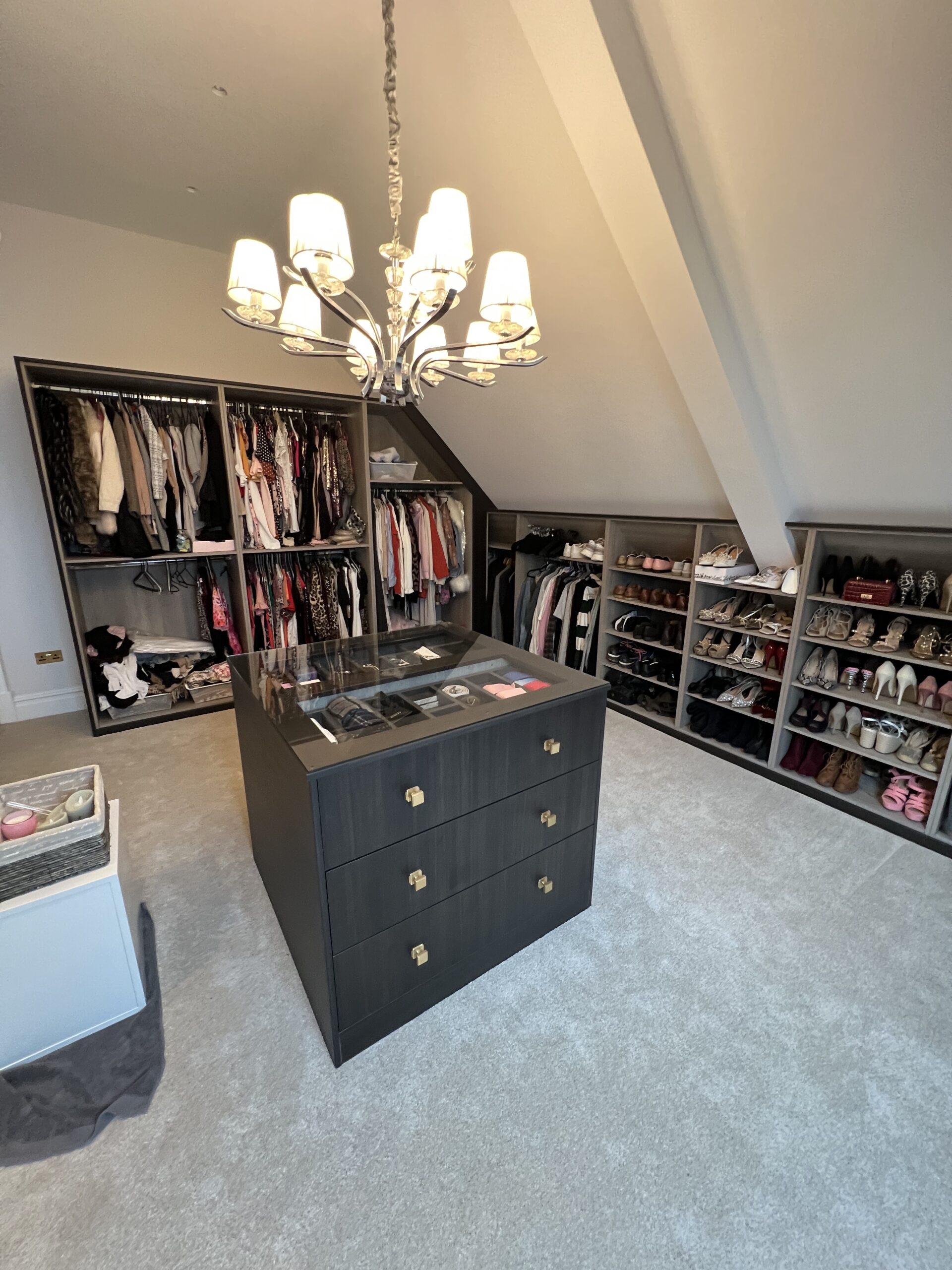 Luxury dressing room in Bredhurst with a glass-topped island, open hanging wardrobes and shoe storage under a sloping ceiling