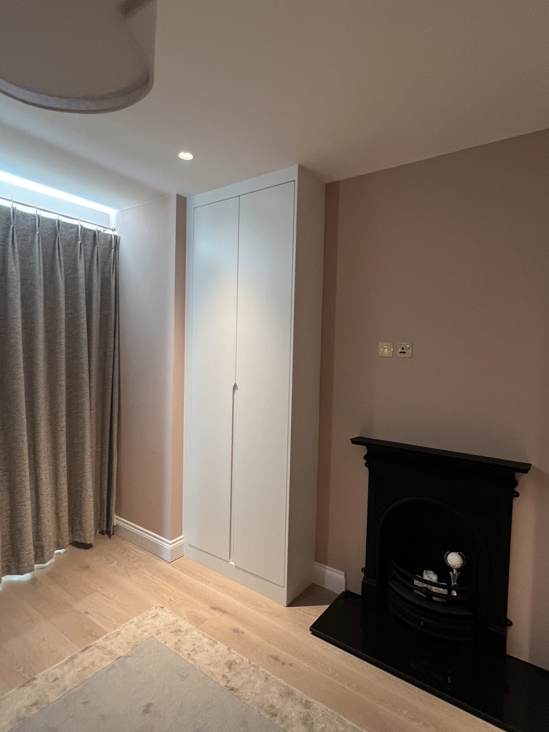 Tall Pure White fitted wardrobe with custom J-pull doors beside a black fireplace in the renovated Battersea bedroom