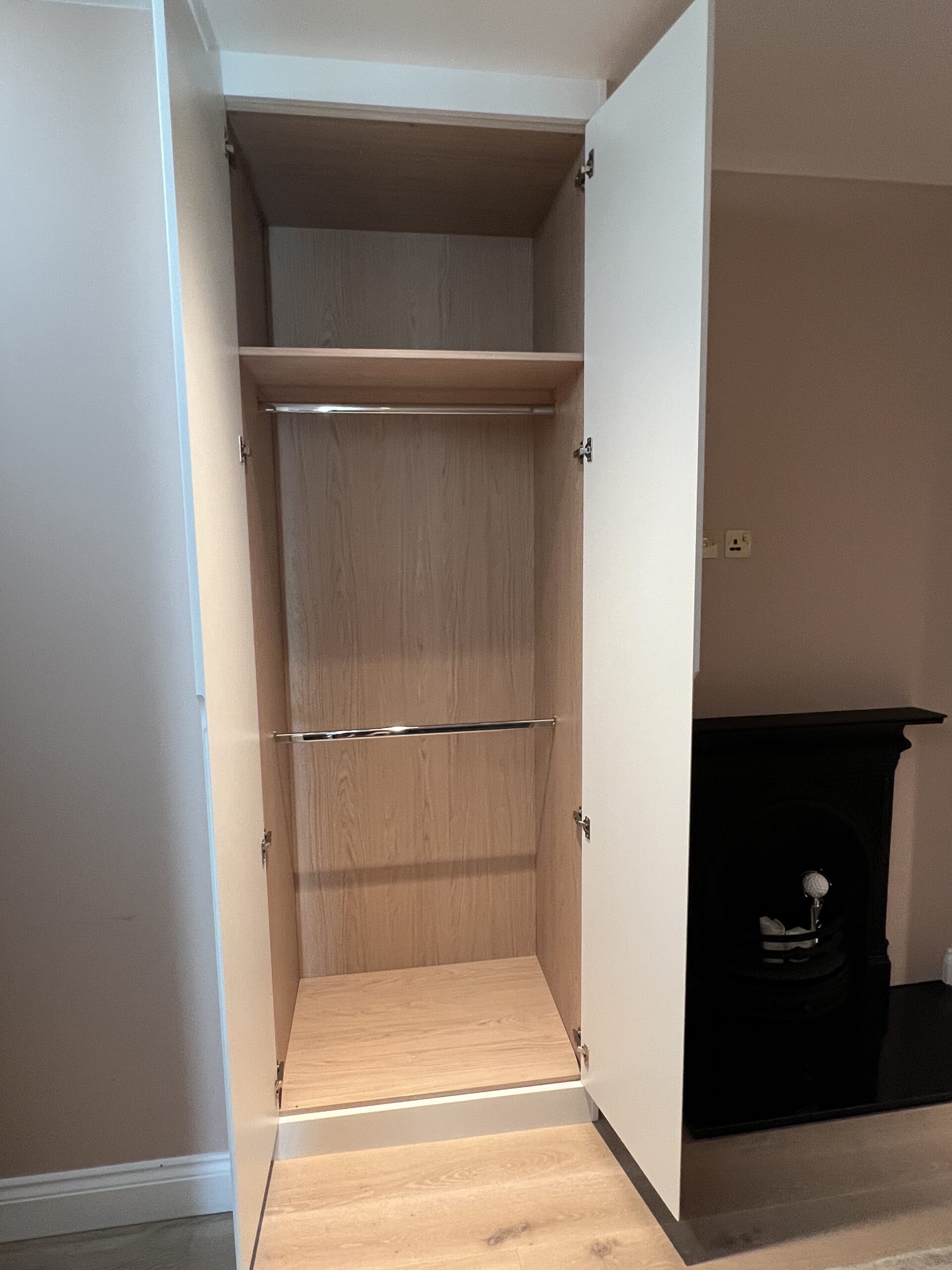 Open Pure White fitted wardrobe showing Egger Light Natural Casella Oak interior with a top shelf and double hanging rails in Battersea